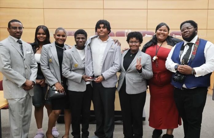 A group photo of the Henry Ford High School Debate Team standing together indoors after the win
